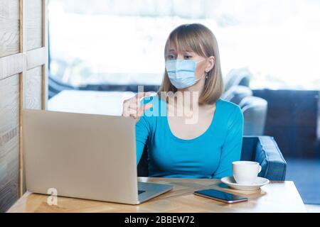 Ho bisogno di un po' di più. Ritratto di donna preoccupata con maschera medica chirurgica seduta e lavoro su laptop su video chiamata e chiedere di più smothing Foto Stock