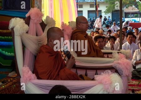 Kambot, Cambogia, Asia: Due monaci buddisti seduti in poltrona parlano con una folla di fedeli Foto Stock