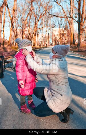 Donna mettere una maschera sul viso della sua bambina. Mamma e sua figlia indossano le maschere facciali per evitare infezioni da virus e prevenire la diffusione della malattia. Foto Stock