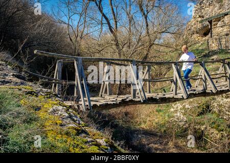 Le donne caucasiche che attraversano sopra un vecchio uomo di rickety inaffidabile hanno fatto il ponte del piede di legno sopra una gola del fiume. Gorge uomini Bulgaria Foto Stock