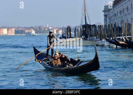 Venezia, Italia-Febbraio 2020; primo piano di un gondoliere con alcuni clienti nel tardo pomeriggio sole sullo sfondo della laguna di Venezia Foto Stock