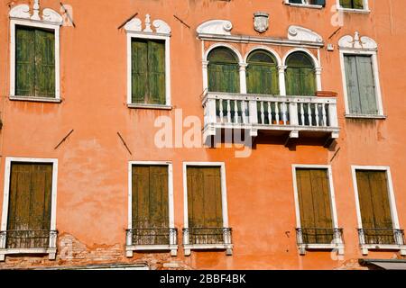 Vista ravvicinata di una sezione di uno degli edifici storici di Venezia con un gran numero di persiane stagne contro un muro con un po' di col sbiadito Foto Stock