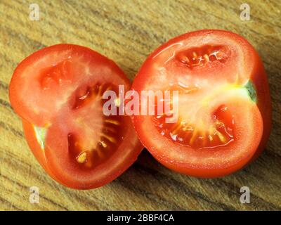 Un pomodoro tagliato a metà su un tagliere di legno Foto Stock