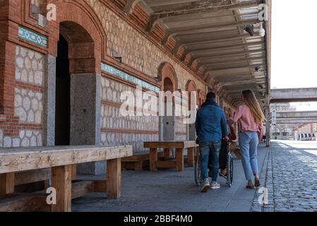 Un giovane latino-americano paralizzato in carrozzina accompagnato da una giovane ragazza caucasica e latino-americana che passeggiando felicemente per la strada Foto Stock