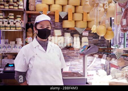 Un assistente del negozio di formaggi che indossa una maschera protettiva covid-19. Milano, Italia - Marzo 2020 Foto Stock