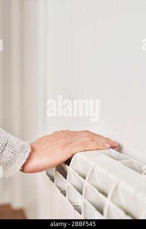 primo piano di un uomo caucasico, con un maglione grigio chiaro, toccando un radiatore ad acqua calda per controllarne la temperatura o riscaldare la mano Foto Stock