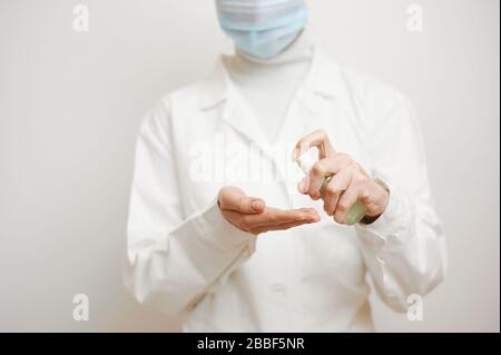 Vista ravvicinata delle mani dei medici femminili utilizzando un antisettico o un igienizzatore personale. Medico in abito medico bianco su sfondo bianco pulito. Foto Stock