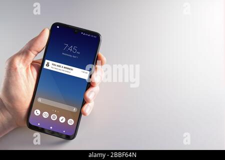 Mano maschile che tiene uno smartphone con notifica del vincitore della lotteria il mese di aprile 1st. Truffa, sciocchi di aprile, criminalità informatica, privacy e concetti tecnologici. Foto Stock