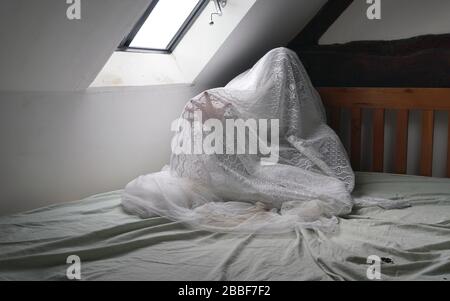 Una figura spettrale e spettrale seduta su un letto, con una mano che raggiunge fuori nel dolore Foto Stock