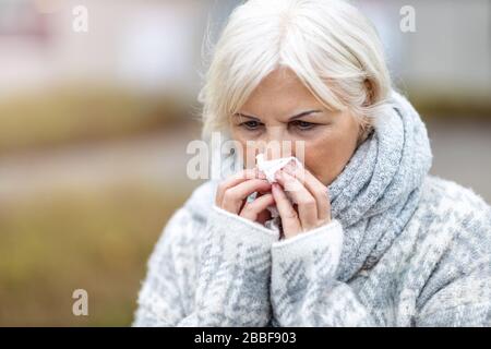 Donna anziana ammalata che soffia il naso Foto Stock
