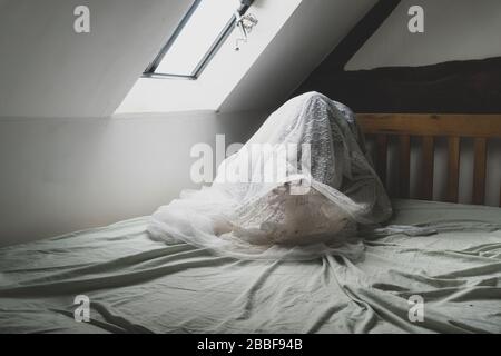 Una figura spettrale e spettrale seduta su un letto, con una mano che arriva Foto Stock