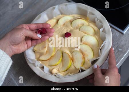 La padrona di casa sta preparando la mela charlotte in cucina. Mette il bacche su una torta di mele in un piatto da forno. Pasta di mele cruda Foto Stock