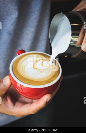 Barista che versa il latte dalla caraffa per preparare la latte da caffè Foto Stock