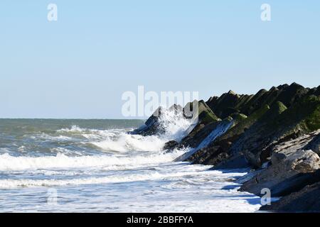 Vista su una fila di grandi blocchi di cemento estremi che fungono da breakwater sulla spiaggia di Maasvlakte vicino a Rotterdam; onde che si infrangono contro i blocchi Foto Stock