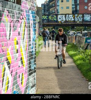 Un ciclista che guarda il suo telefono mentre si guida su un percorso lungo il fiume a Hackney Wick, Londra orientale Foto Stock