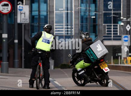 Birmingham, West Midlands, Regno Unito. 31st marzo 2020. Un pilota deliveroo passa un addetto al supporto della comunità di polizia nel centro di Birmingham durante il blocco pandemico di Coronavirus. Credit Darren Staples/Alamy Live News. Foto Stock