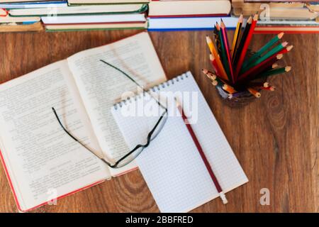 Libro di testo aperto, notebook, occhiali, matite nel supporto, stack di vecchio libro su tavola di legno, istruzione concetto di fondo, molti libri pile con spazio di copia Foto Stock