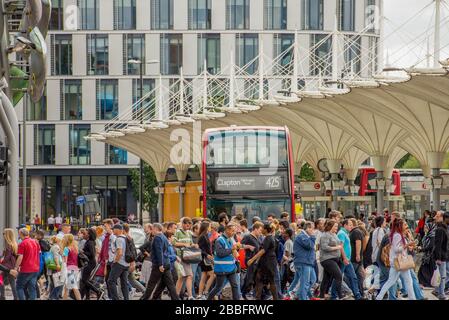 Una folla di amanti dello shopping attraversa la strada tra la stazione ferroviaria di Stratford e il centro commerciale Stratford Centre in una giornata estiva soleggiata. Un autobus di Londra aspetta. Foto Stock