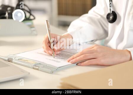 Primo piano di mani medico donna che riempiono record clinici seduto su una scrivania in ufficio Foto Stock