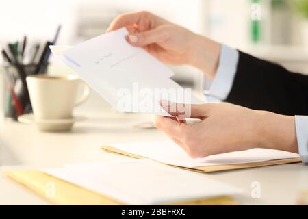 Primo piano di lavoro donna mano mettere lettera su una busta seduta su una scrivania in ufficio Foto Stock