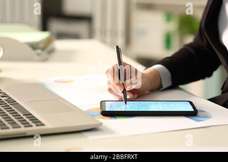 Primo piano di mani executive donna compilare il documento con lo stilo su smartphone su una scrivania in ufficio Foto Stock