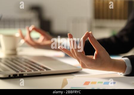 Primo piano delle mani esecutive stress alleviando fare yoga posa di notte seduta su una scrivania in ufficio Foto Stock