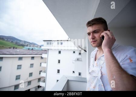 Pittore che fa la chiamata telefonica mentre si alza sul balcone durante la pausa dal decoratore di lavoro Usando il telefono mobile in piedi Fuori Foto Stock