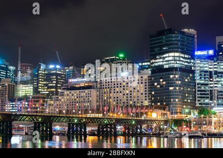 Darling Harbour a Sydney, Australia di notte con il ponte pedonale Pyrmont Bridge visibile. Serata al porto con diverse gru a torre. Foto Stock