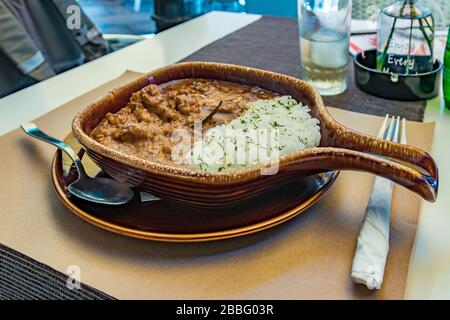 cena appetitosa con riso con salsa e goulash di carne. Cibo gustoso e salutare a base di prodotti naturali. Tavolo da ristorante, pato di ceramica e bicchiere di whi Foto Stock