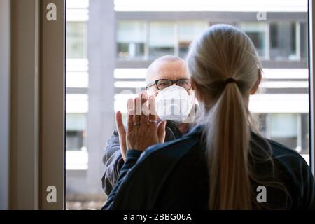 Una coppia sposata separata dal virus Corona Covid-19. È messa in quarantena all'interno ed è all'esterno indossando una maschera protettiva. Stanno tenendo le mani thro Foto Stock