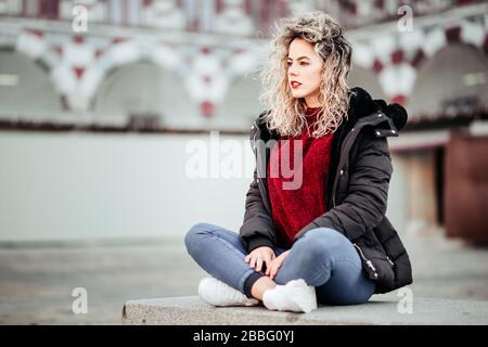 donna bionda curly seduta su bech. Abbigliamento casual Foto Stock