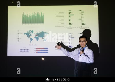 Giovane scienziato medico asiatico fiducioso che punta allo schermo di proiezione mentre parla di soluzione di coronavirus durante la riunione Foto Stock