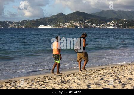 Grenada locale a piedi sulla spiaggia di Grand Anse e nave da crociera a St Georges sullo sfondo Foto Stock