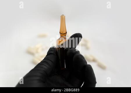 Mano nel guanto in lattice nero che tiene un ampolle di vetro per uso medico con il medicinale Foto Stock
