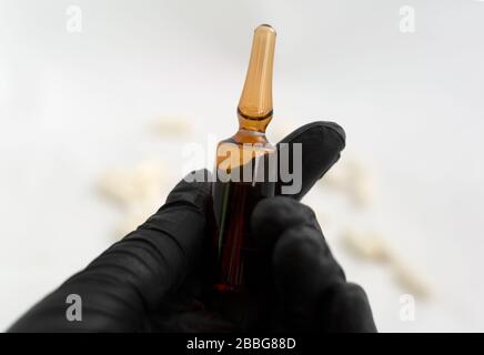 Mano nel guanto in lattice nero che tiene un ampolle di vetro per uso medico con il medicinale Foto Stock