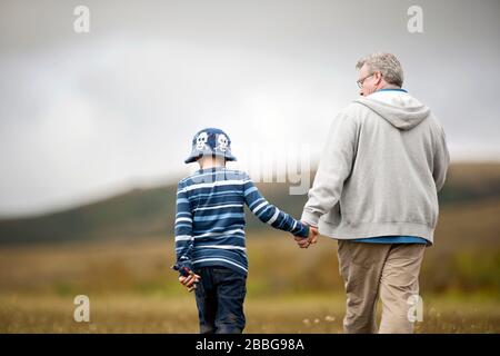 Ragazzo giovane che cammina attraverso un campo con suo nonno Foto Stock