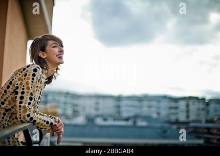 Ritratto di una bella giovane donna che si affaccia su un balcone che si affaccia sulla città Foto Stock