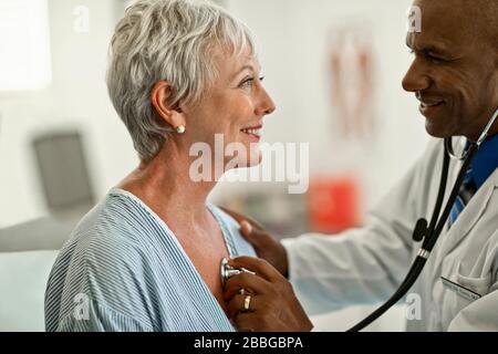 Donna matura allegro che ha il suo battito cardiaco controllato da un medico amichevole Foto Stock