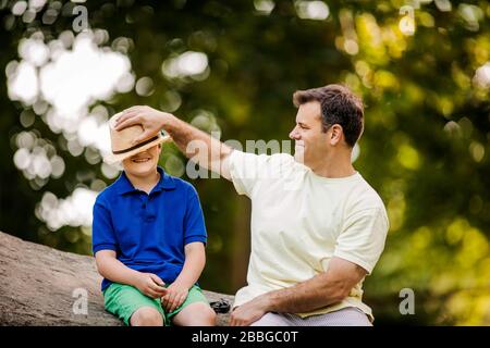 Sorridente padre che ha messo un cappello di paglia sulla testa di suo figlio Foto Stock