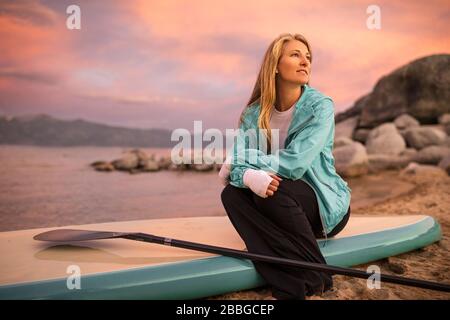 Giovane donna seduto sulla sua tavola da paddle Foto Stock