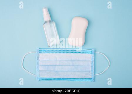 Igiene delle mani del viso. Top flatlay primo piano foto di spray antibatterico bianco sapone solido e maschera chirurgica isolato su sfondo blu Foto Stock