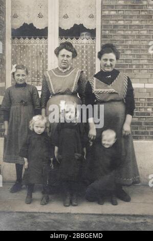 Stretphoto vintage di 2 donne e bambini ragazze di classe operaia ad Anversa e un uomo starnutisce attraverso la finestra di una casa. Belgio Foto Stock