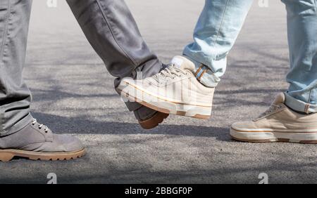 Battendo con i piedi. Un nuovo saluto per evitare la diffusione del coronavirus. Due amici si incontrano, invece di salutarsi con un abbraccio o una stretta di mano, a Foto Stock