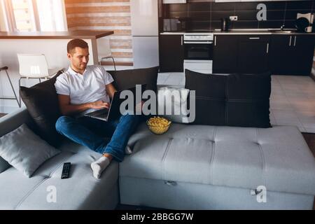 Giovane uomo guarda la tv nel suo appartamento. Felice positivo uomo lavoro su laptop. Telecomando fuori ufficio. La persona che lavora duro ha divertimento e. Foto Stock