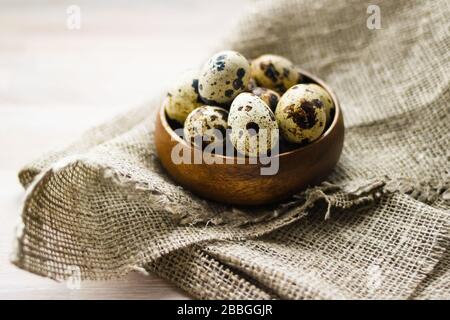 Uova di quaglia in ciotola rotonda di bambù su tela del sacco su fondo di legno. Mangiare sano, concetto di Pasqua. Foto Stock