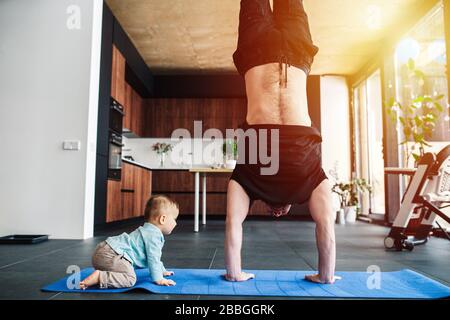 Il Padre esegue un appaio, mentre il suo bambino si gattona sul pavimento Foto Stock