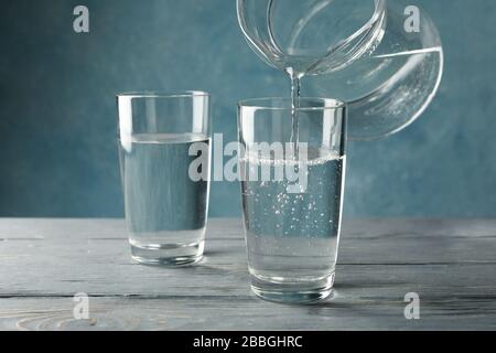 Versare acqua dolce purificata dalla caraffa in vetro su un tavolo di legno Foto Stock