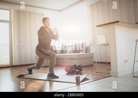 Giovane uomo ordinario va dentro per lo sport nel paese. Immagini luminose di un rinfrescante sportivo concentrato e serio che fa uno squat della gamba con persistenza. Uomo regolare Foto Stock