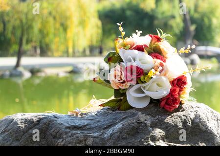 Bouquet di nozze e anelli di fidanzamento si trovano su una roccia. C'è una vista perfetta dietro gli oggetti, il lago e gli alberi. Foto Stock