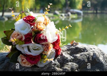 Bouquet di nozze e anelli di fidanzamento si trovano su una roccia. C'è una vista perfetta dietro gli oggetti, il lago e gli alberi. Foto Stock